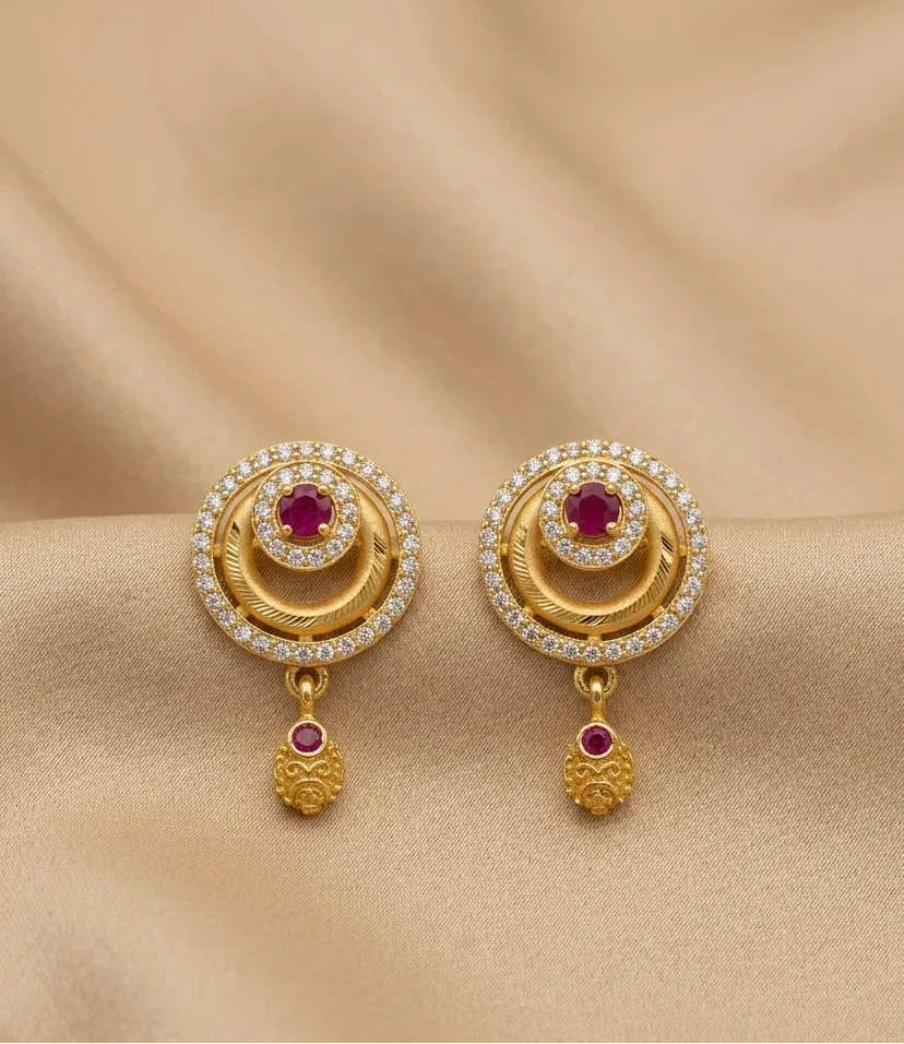 Gold earrings with red gemstones and diamond accents on a beige fabric background