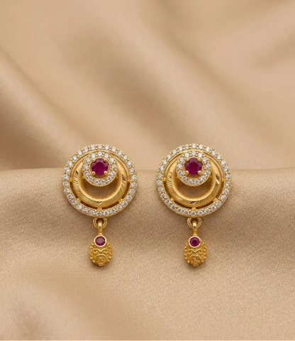 Gold earrings with red gemstones and diamond accents on a beige fabric background