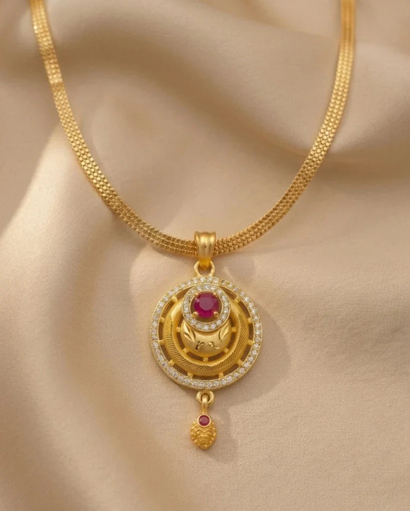Gold necklace with a pendant featuring a red gemstone on a beige fabric background