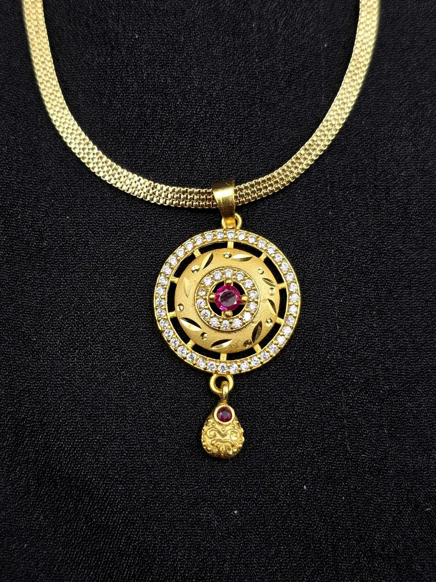 Gold necklace with a circular pendant featuring a red gemstone on a black background