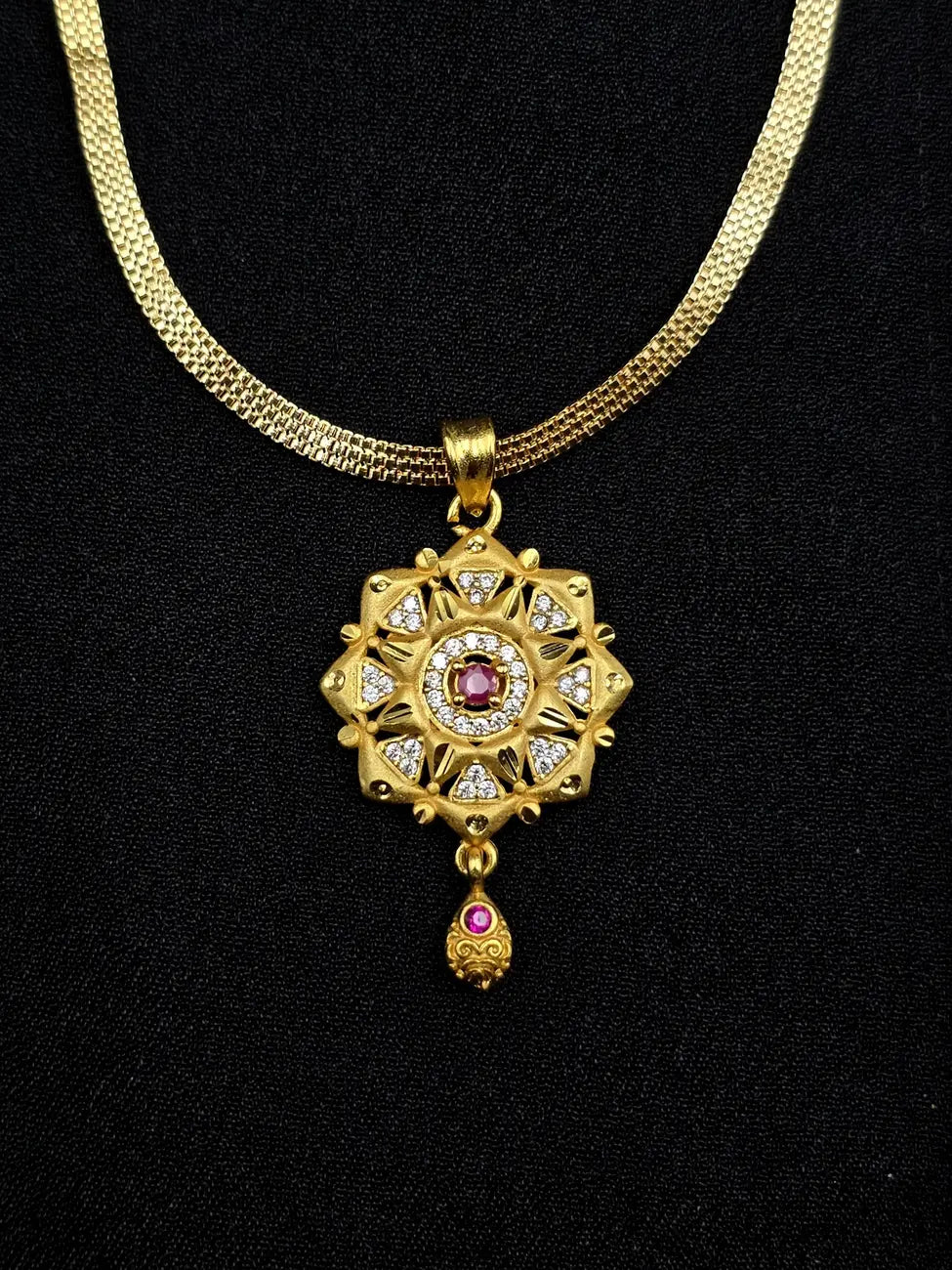 Gold necklace with a decorative pendant featuring rubies and diamonds on a black background