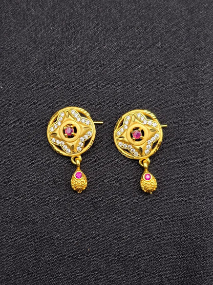Pair of gold earrings with red gemstones on a black background