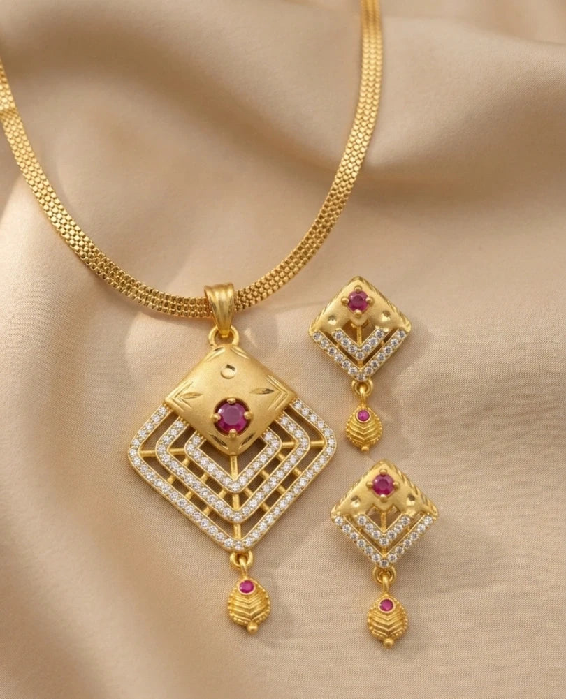 Gold necklace and earrings set with red gemstones on a beige fabric background