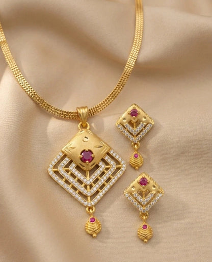 Gold necklace and earrings set with red gemstones on a beige fabric background