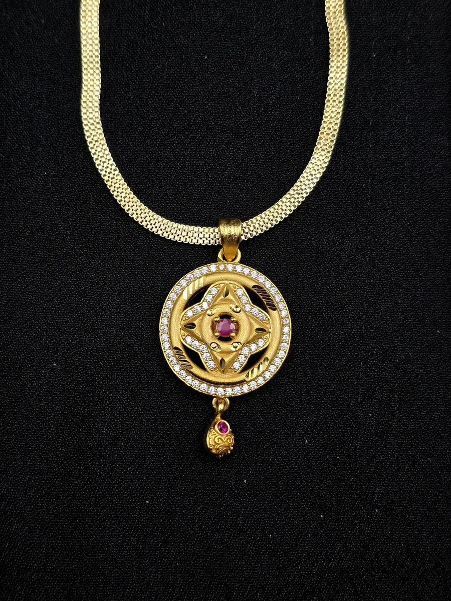 Gold necklace with a pendant featuring a red gemstone on a black background