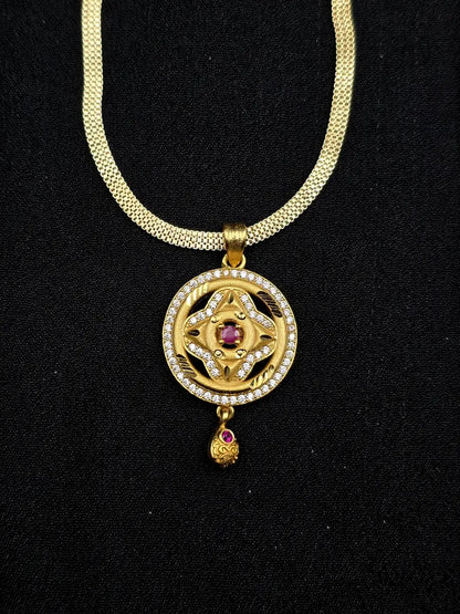 Gold necklace with a pendant featuring a red gemstone on a black background