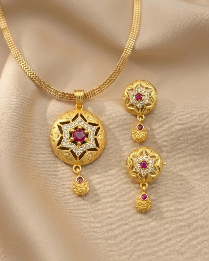 Gold necklace and earrings set with red gemstones on a beige fabric background