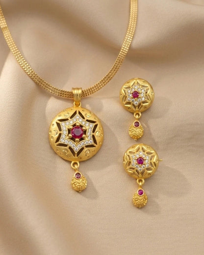 Gold necklace and earrings set with red gemstones on a beige fabric background