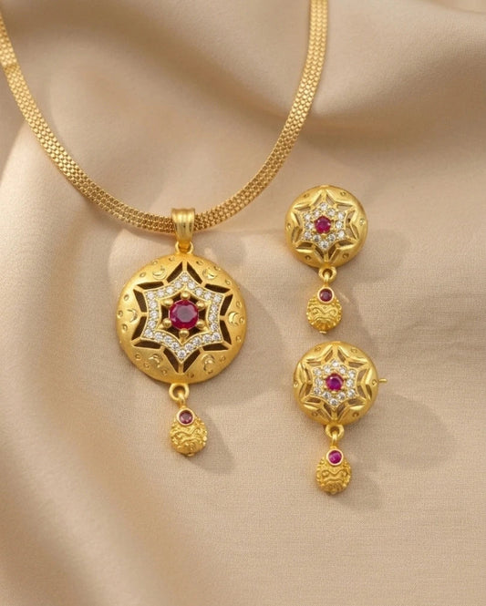 Gold necklace and earrings set with red gemstones on a beige fabric background