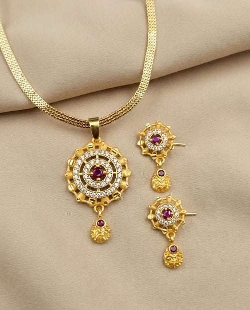 Gold necklace and earrings set with red gemstones on a beige fabric background