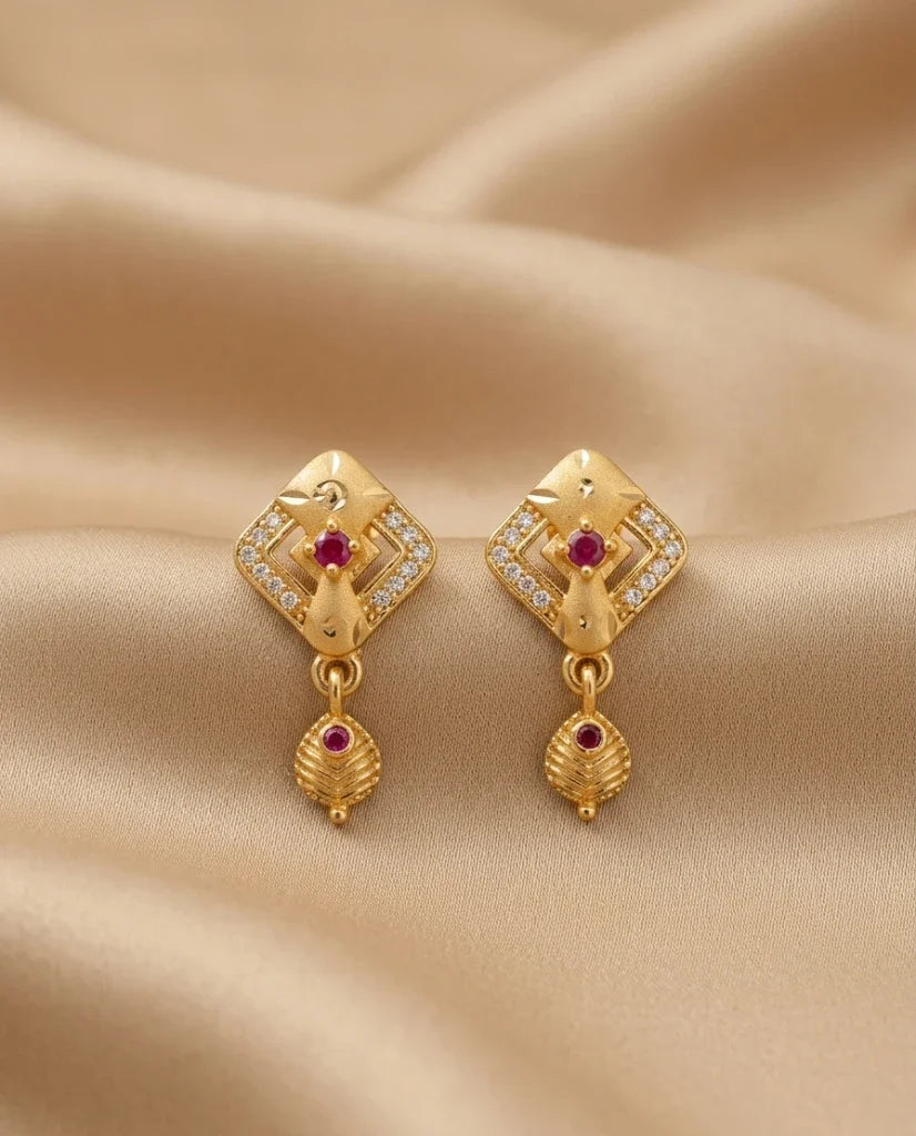 Gold earrings with red gemstones on a beige fabric background