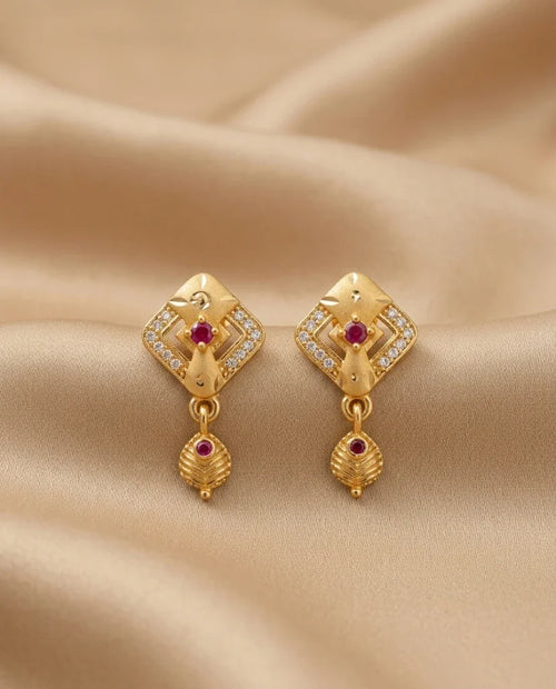 Gold earrings with red gemstones on a beige fabric background