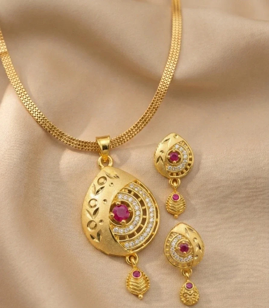 Gold necklace and earrings set with red gemstones on a beige fabric background