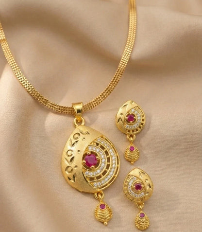 Gold necklace and earrings set with red gemstones on a beige fabric background