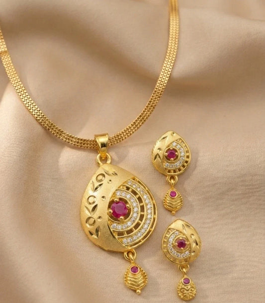 Gold necklace and earrings set with red gemstones on a beige fabric background