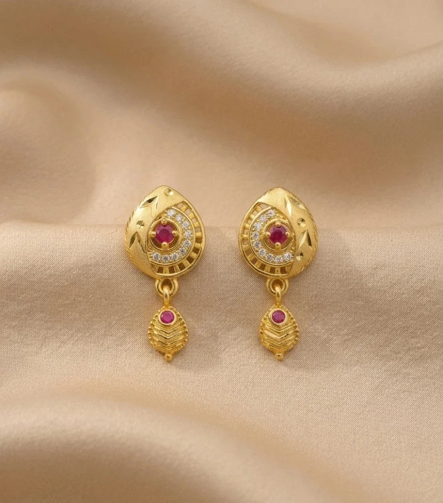 Gold earrings with red gemstones on a beige fabric background