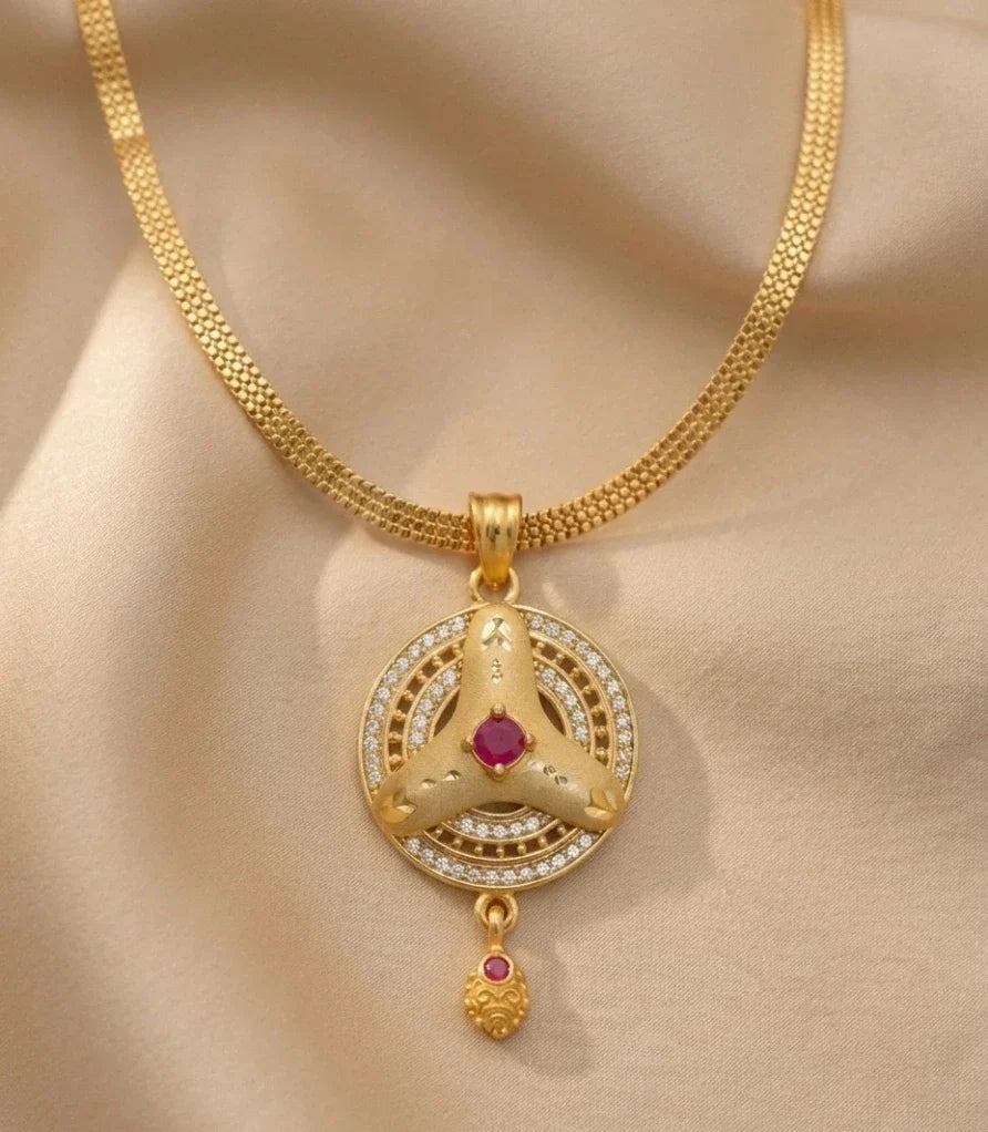 Gold necklace with a circular pendant featuring a red gemstone on a beige fabric background
