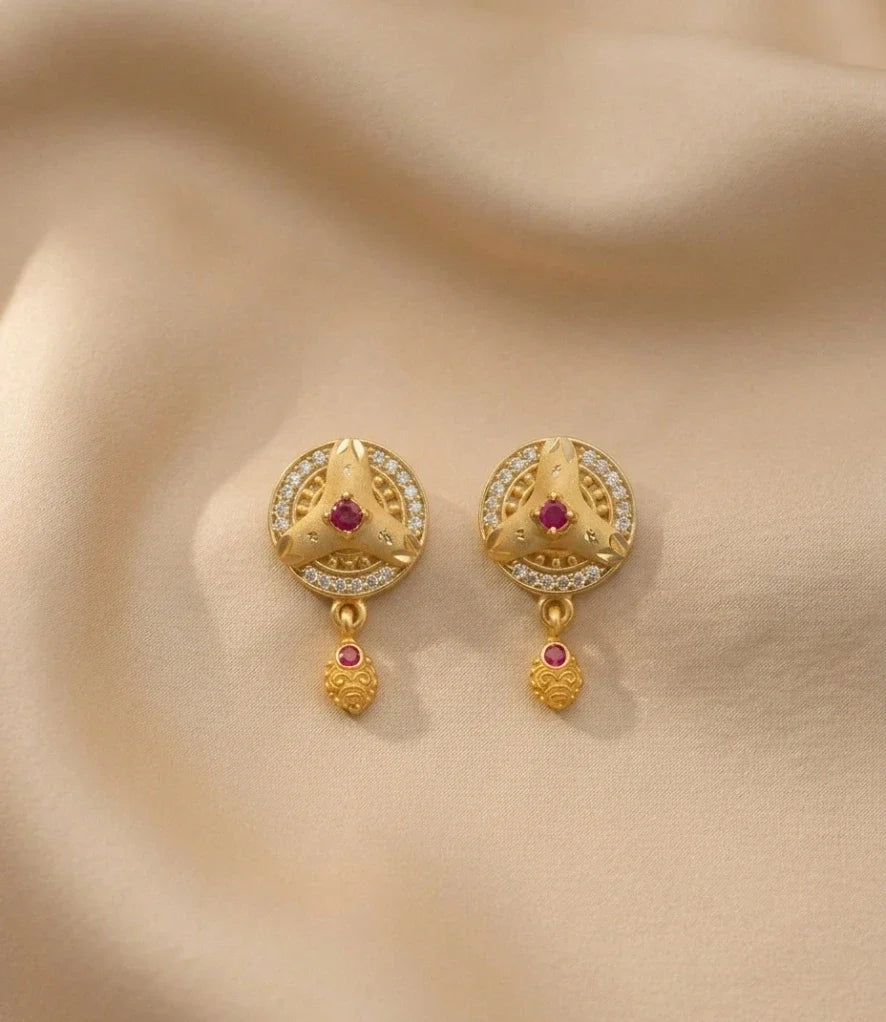 Gold earrings with red gemstones on a beige fabric background