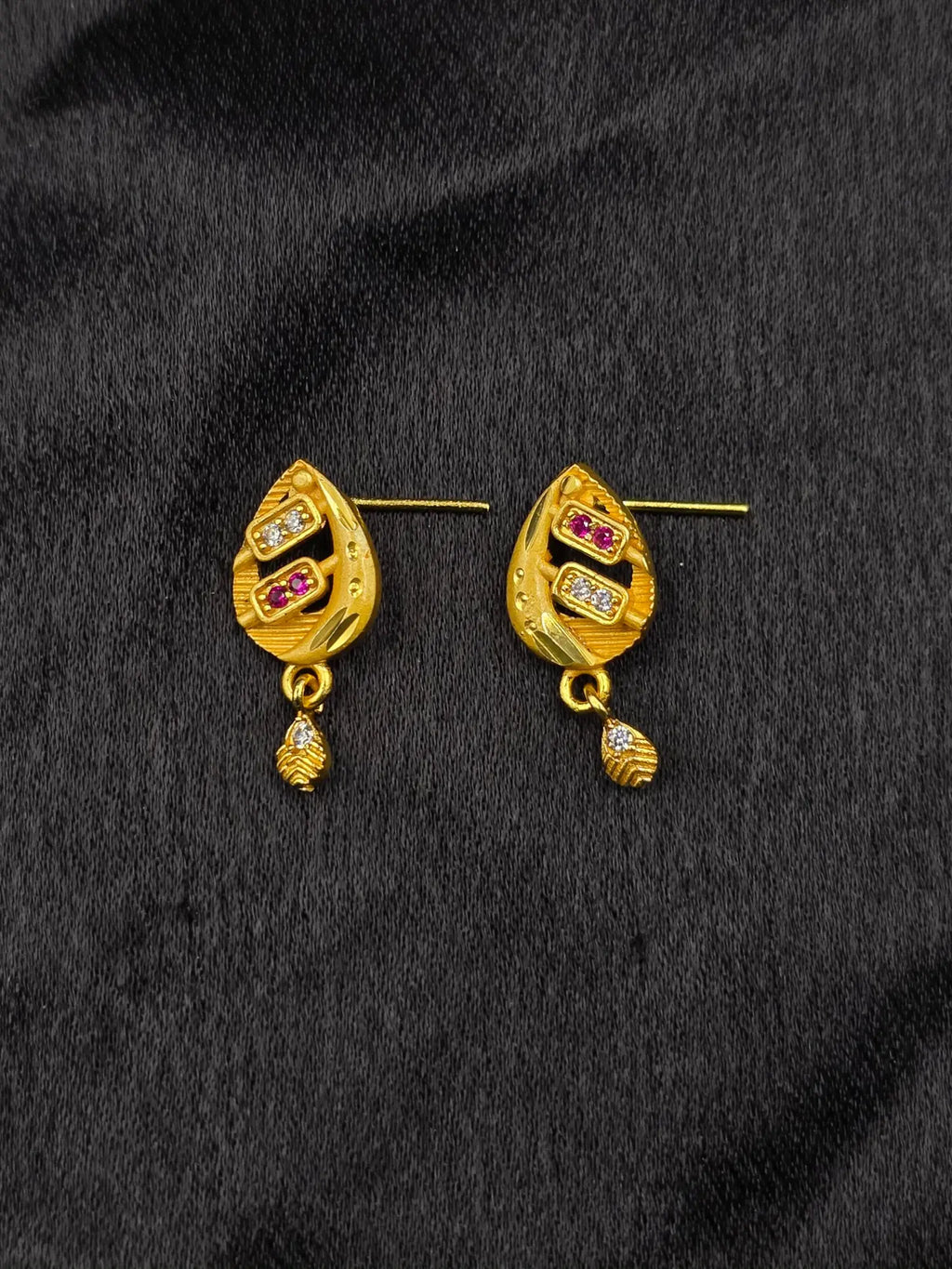 Gold earrings with gemstones on a black fabric background