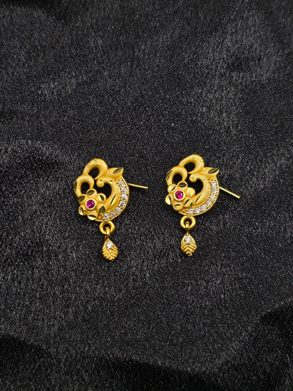 Pair of gold earrings with floral design and red gemstones on a black background