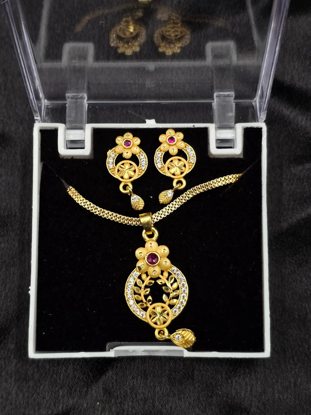 Gold necklace and earrings set in a clear display case on a black background