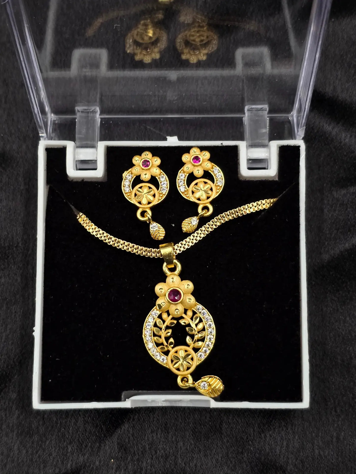 Gold necklace and earrings set in a clear display case on a black background