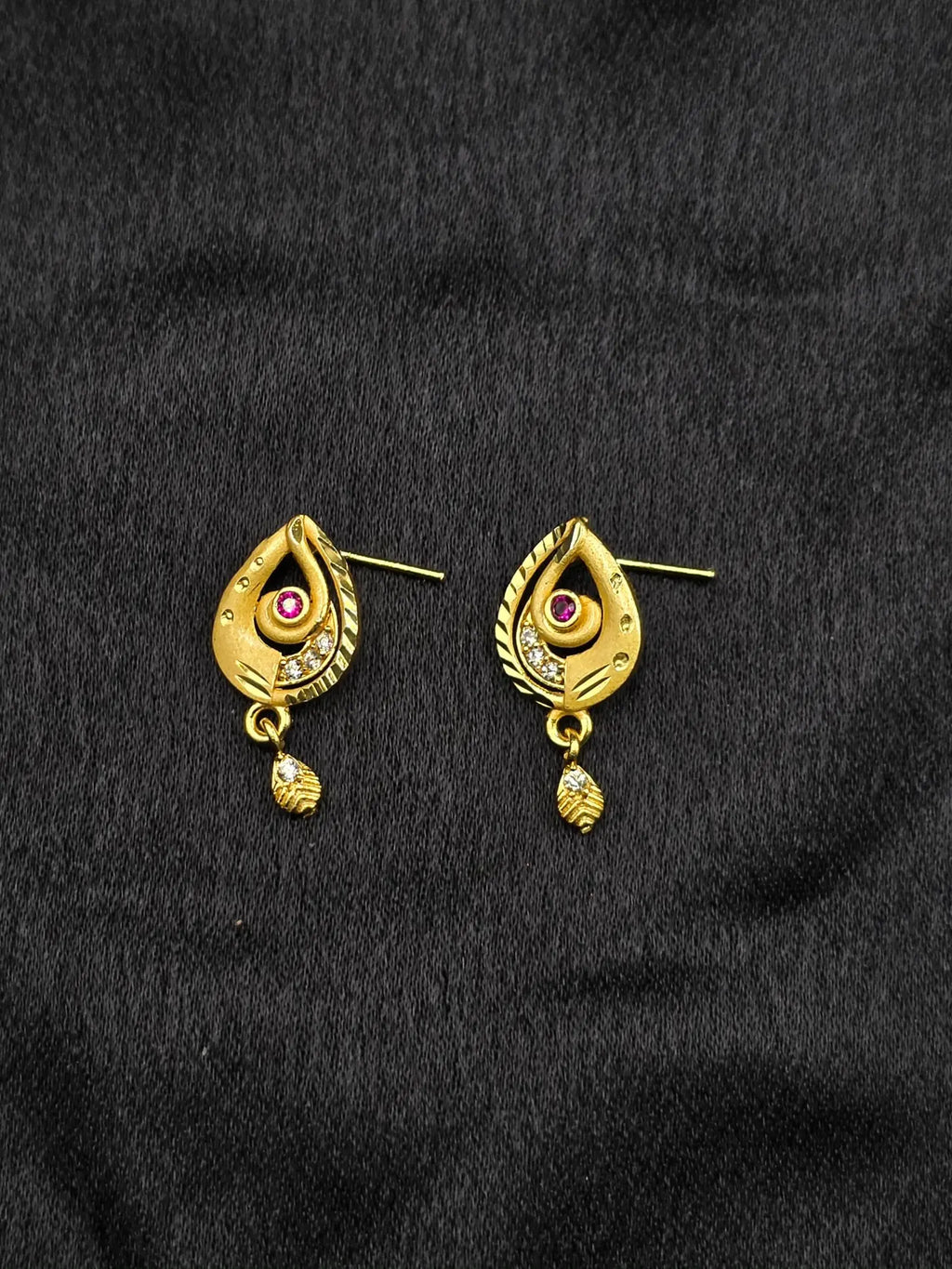 Gold earrings with gemstones on a black fabric background