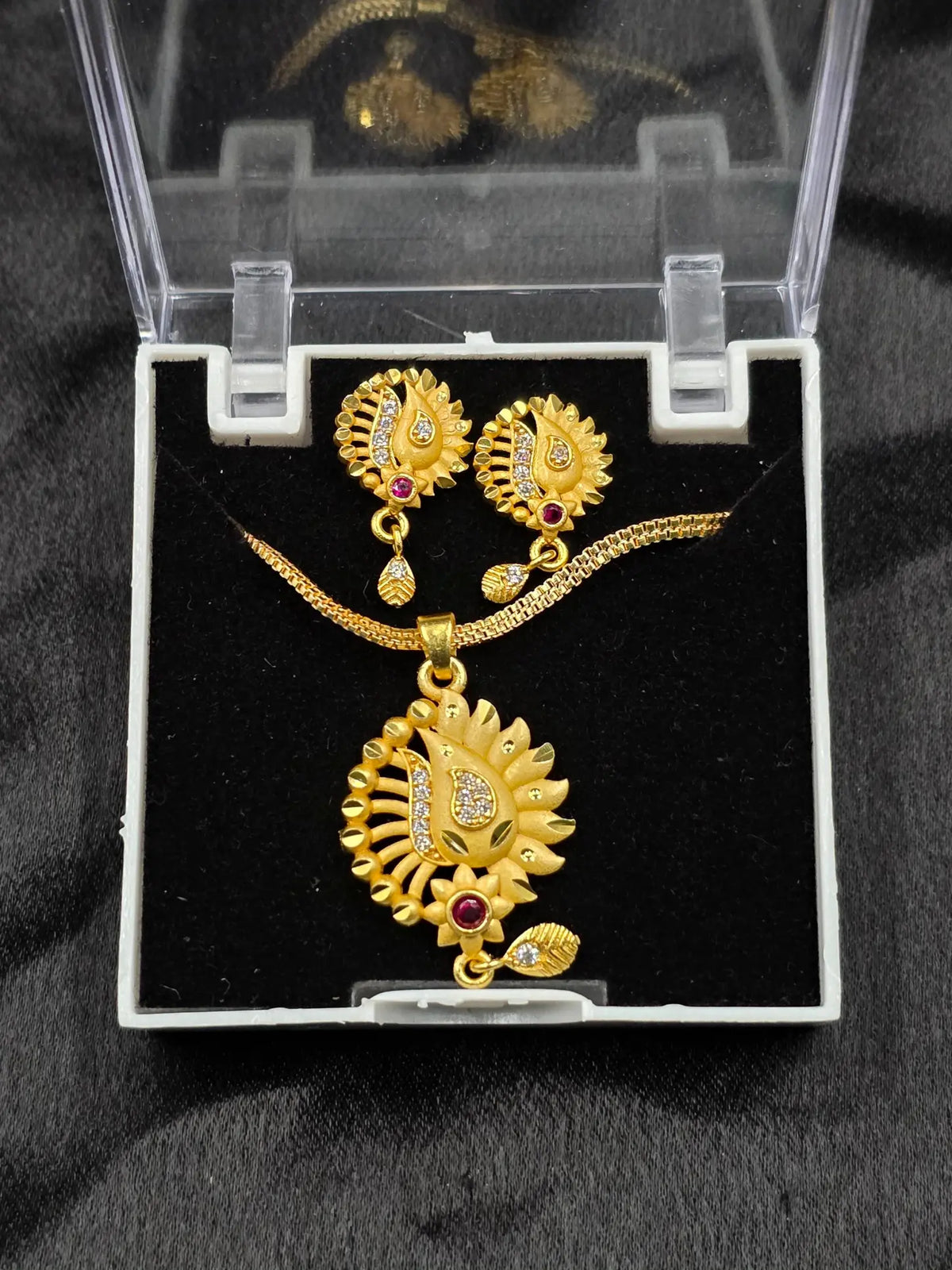 Gold necklace and earrings set in a clear display case on a black background