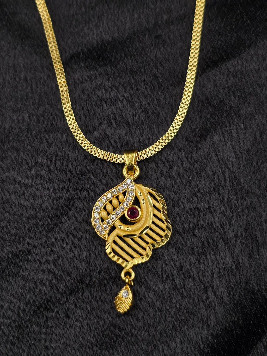 Gold necklace with a pendant featuring a red gemstone on a black background