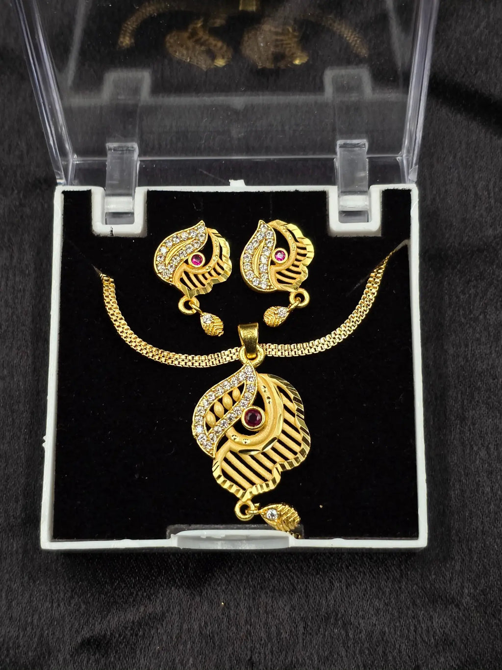 Gold necklace and earrings set in a clear display case on a black background