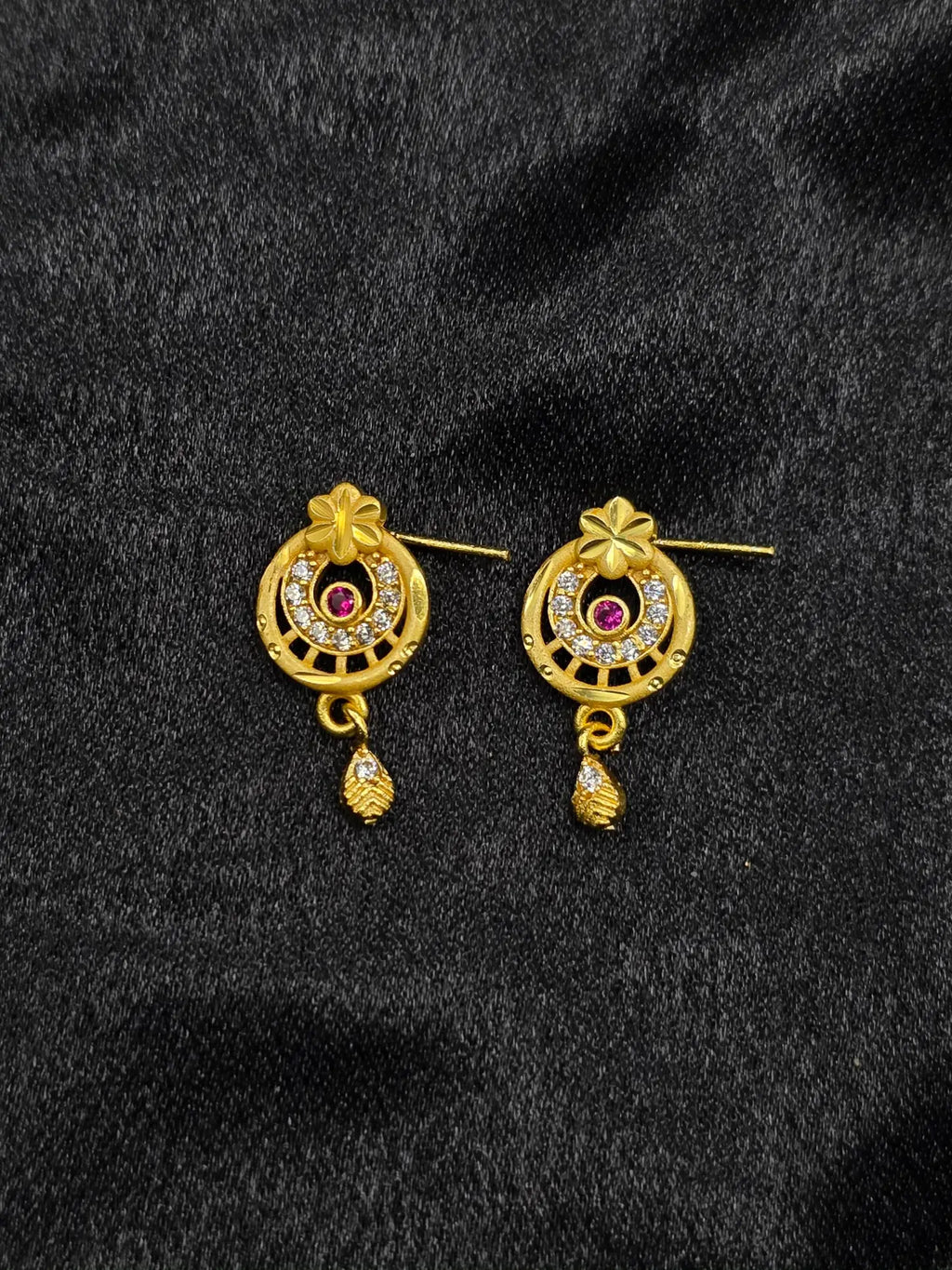 Pair of gold earrings with gemstones on a black fabric background