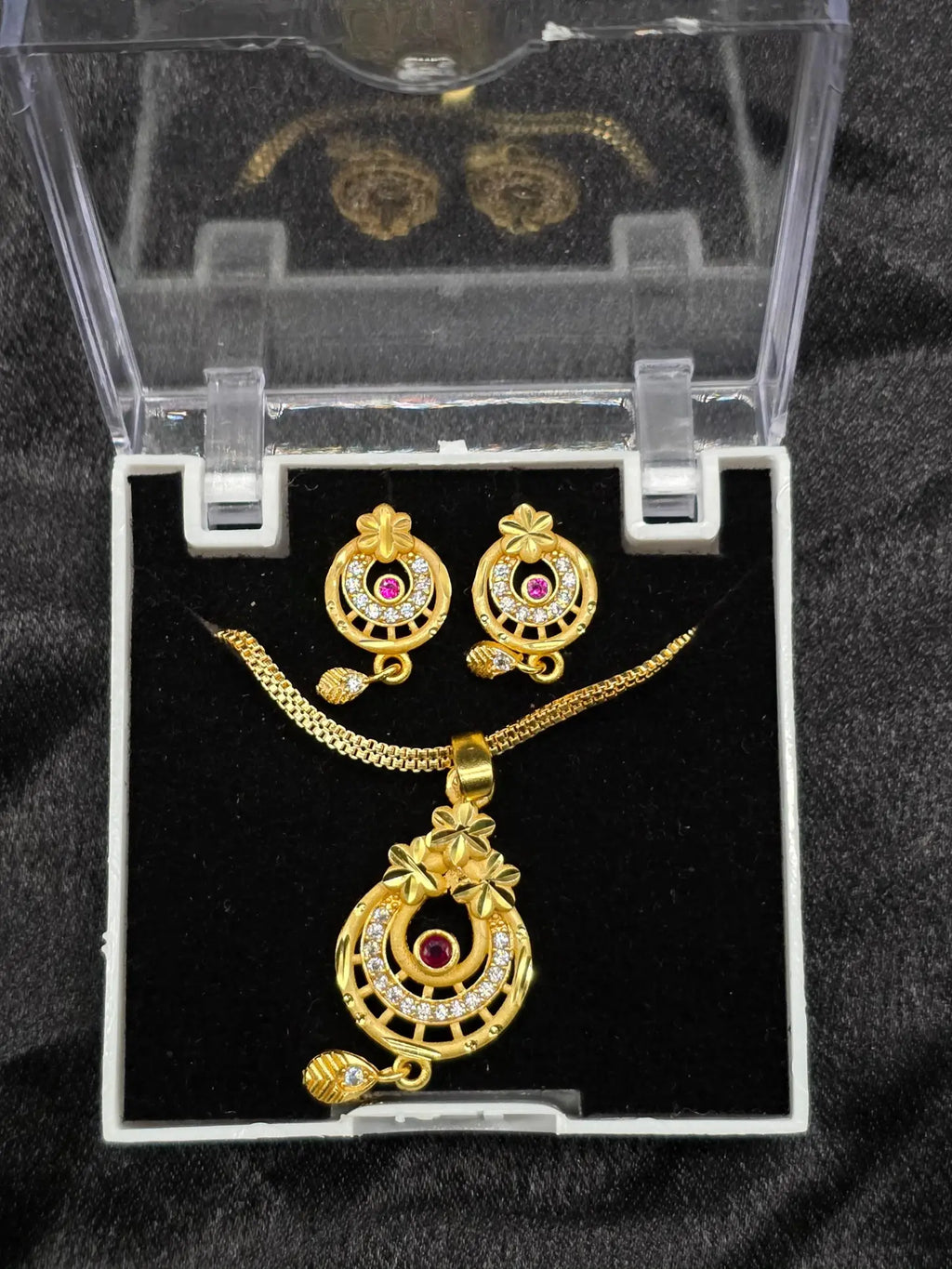 Gold jewelry set with necklace and earrings in a clear box on a black background