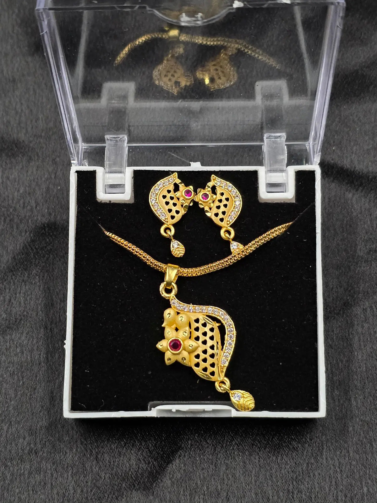 Gold necklace and earrings set in a clear display case on a black background
