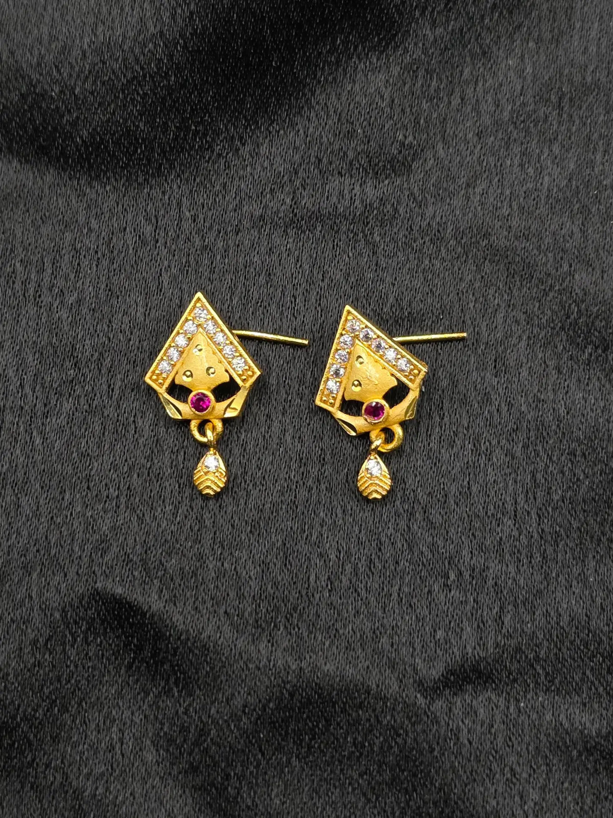 Gold earrings with gemstones on a black fabric background