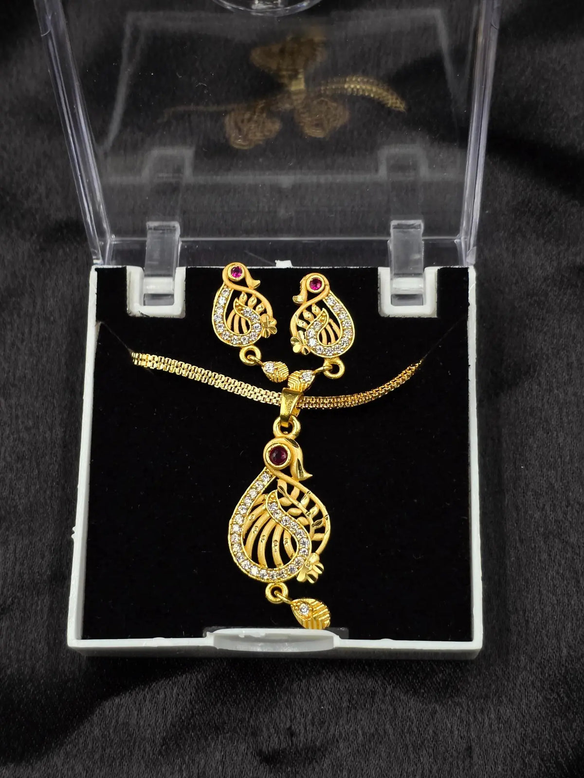 Gold necklace and earrings set in a clear box on a black background