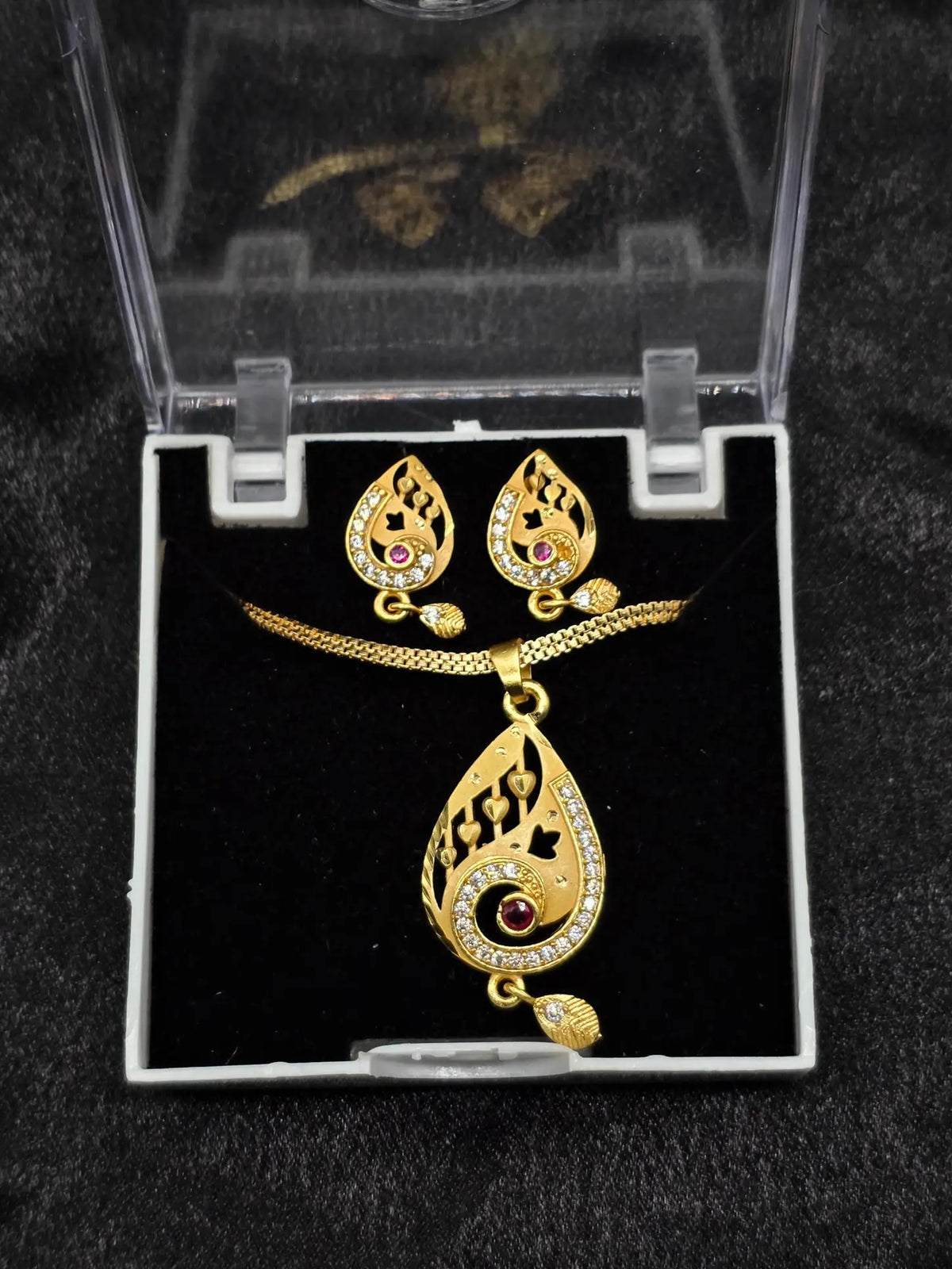 Gold necklace and earrings set in a clear jewelry box on a black background