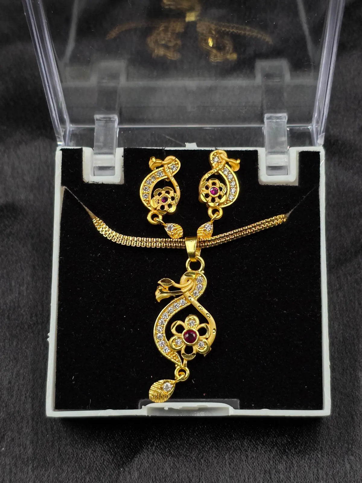 Gold necklace and earrings set on a black cushion with a clear display case.