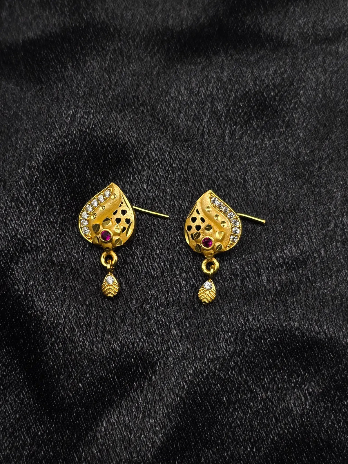 Gold earrings with gemstones on a black fabric background