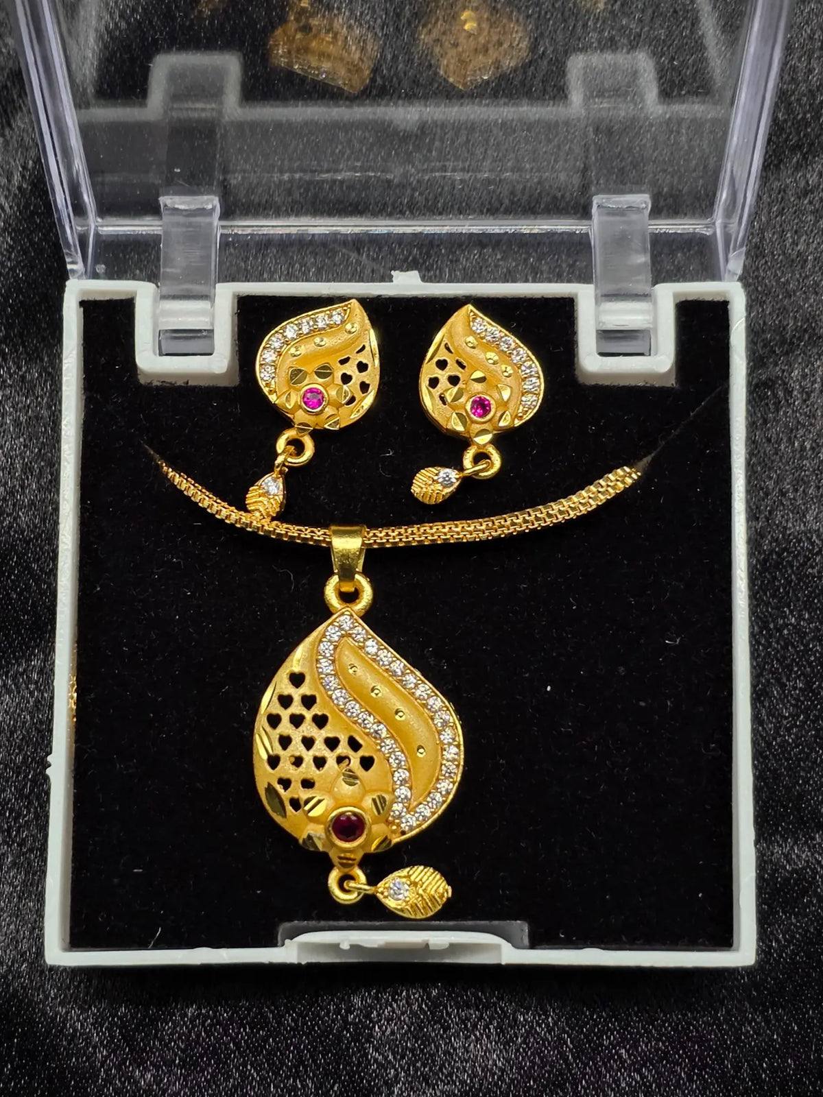 Gold necklace and earrings set in a clear display case on a black background