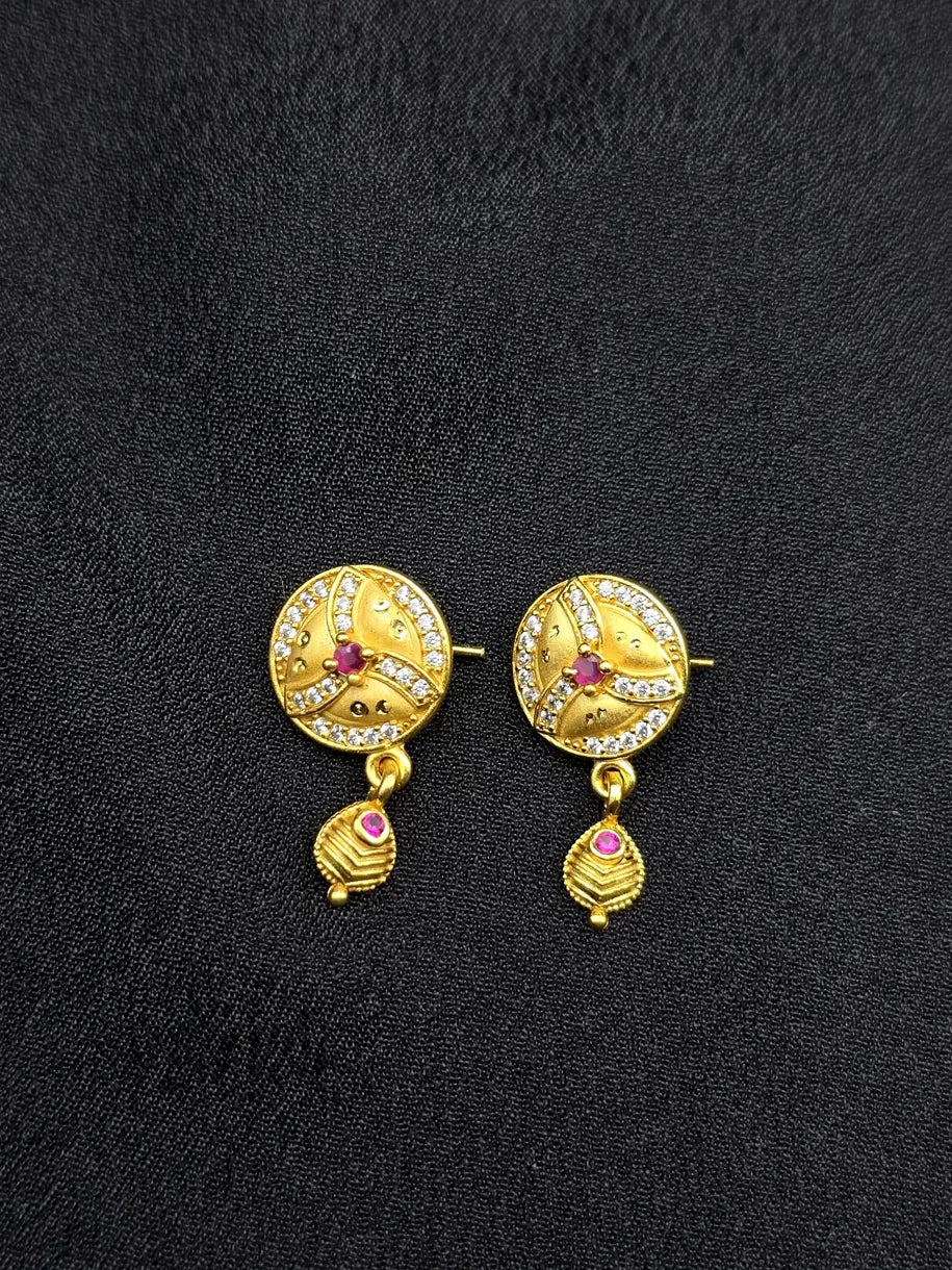 Gold earrings with red gemstones on a black fabric background