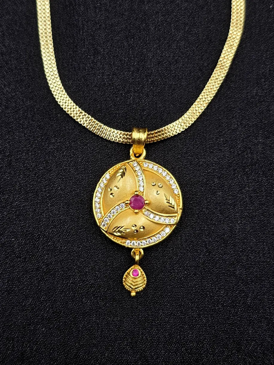 Gold necklace with a circular pendant featuring a red gemstone on a black background