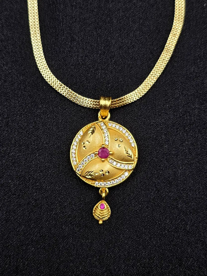 Gold necklace with a circular pendant featuring a red gemstone on a black background