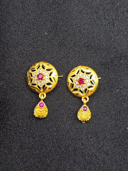 Gold earrings with red gemstones and diamond-like stones on a black background