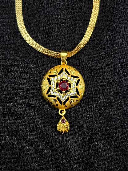 Gold necklace with a star-shaped pendant featuring a red gemstone on a black background