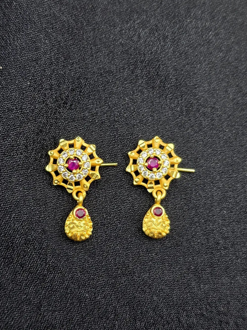 Pair of gold earrings with red gemstones on a black background