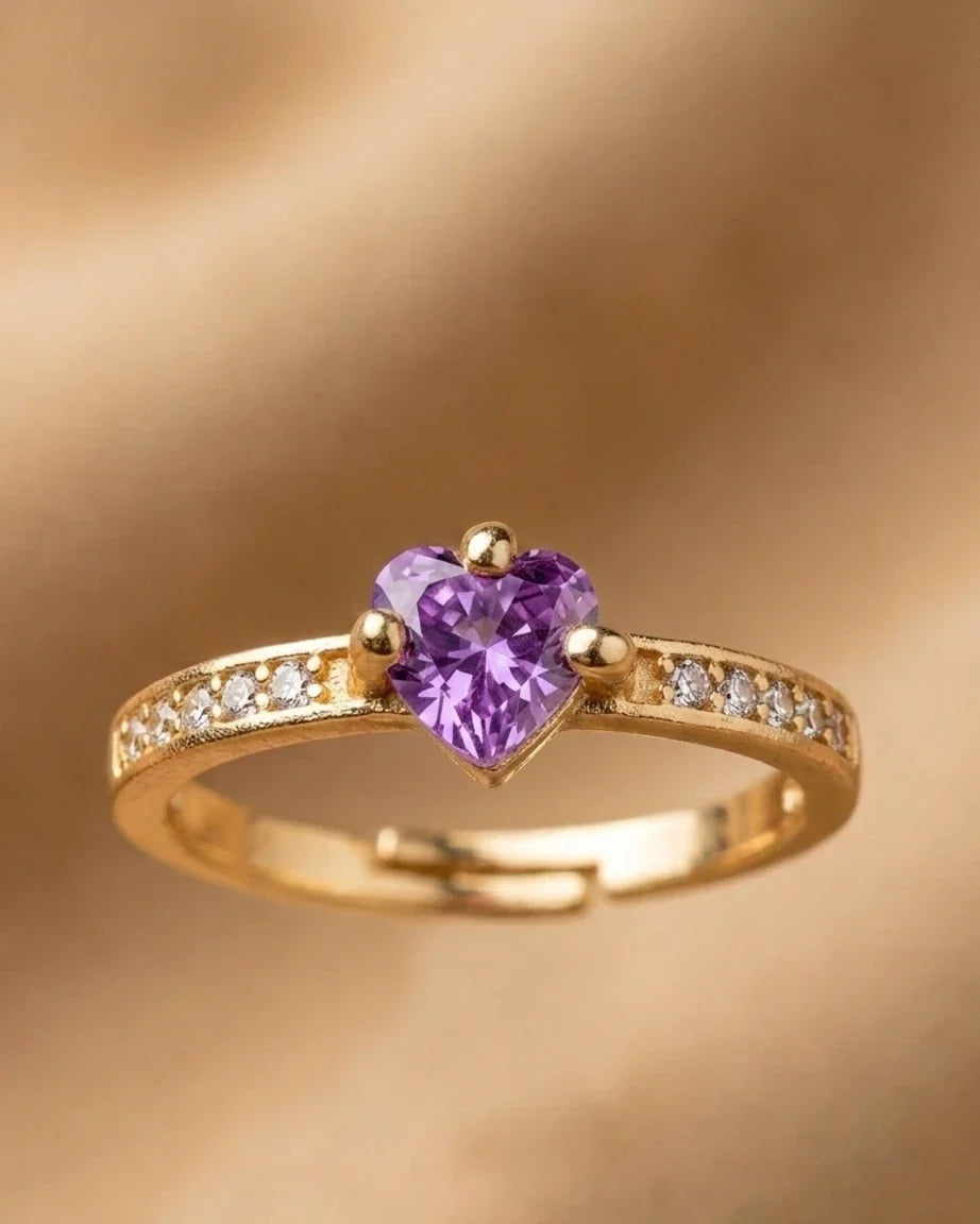 Gold ring with a heart-shaped purple gemstone on a gold background