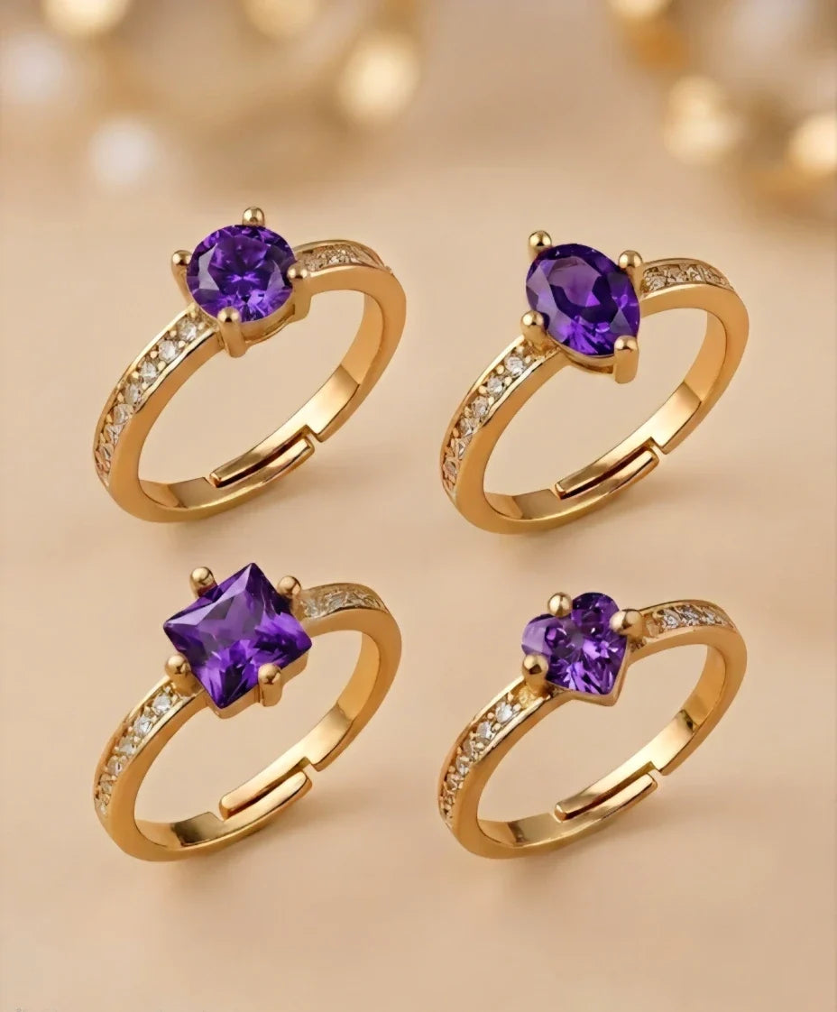 Four gold rings with purple gemstones on a beige background