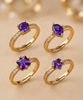 Four gold rings with purple gemstones on a beige background
