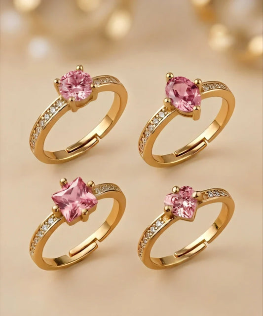 Four gold rings with pink gemstones on a beige background