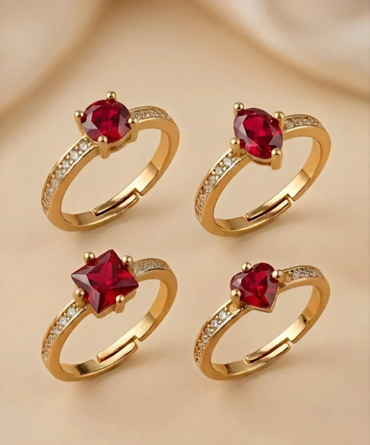 Four gold rings with red gemstones on a beige background